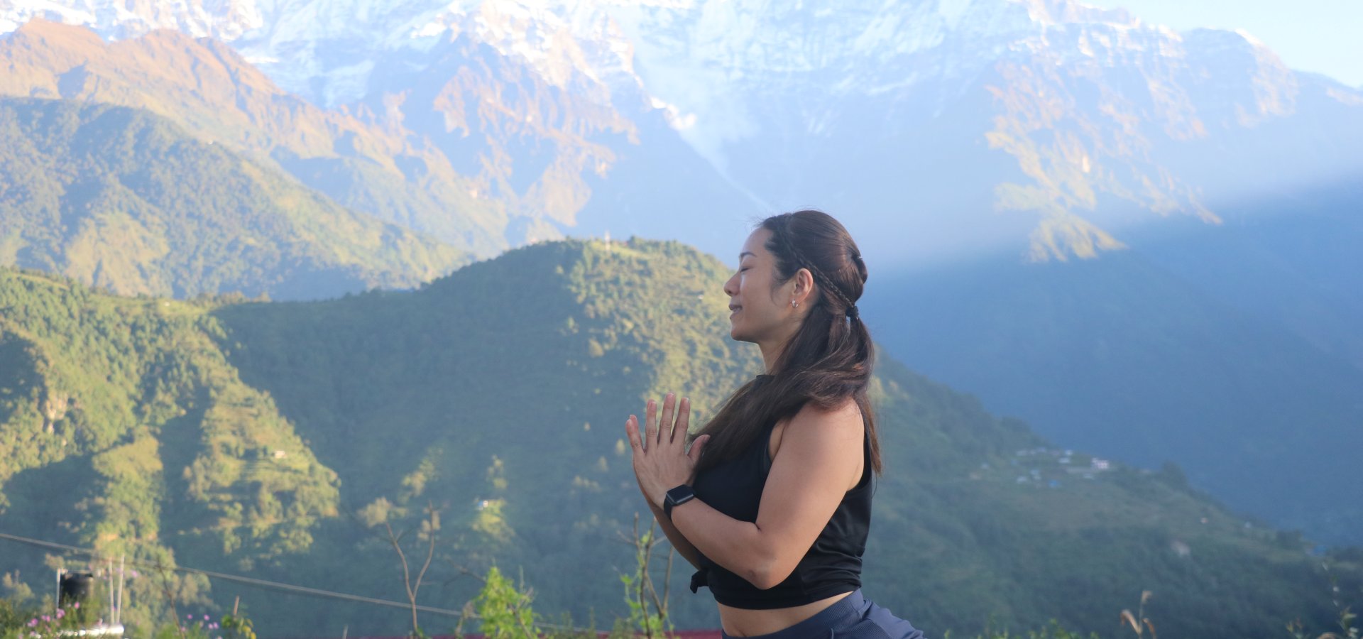 Person meditating on a wooden deck overlooking misty Himalayan mountains at sunrise.